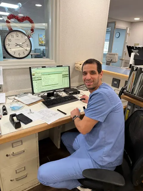 Joan Morales seated at a healthcare workstation in nursing scrubs